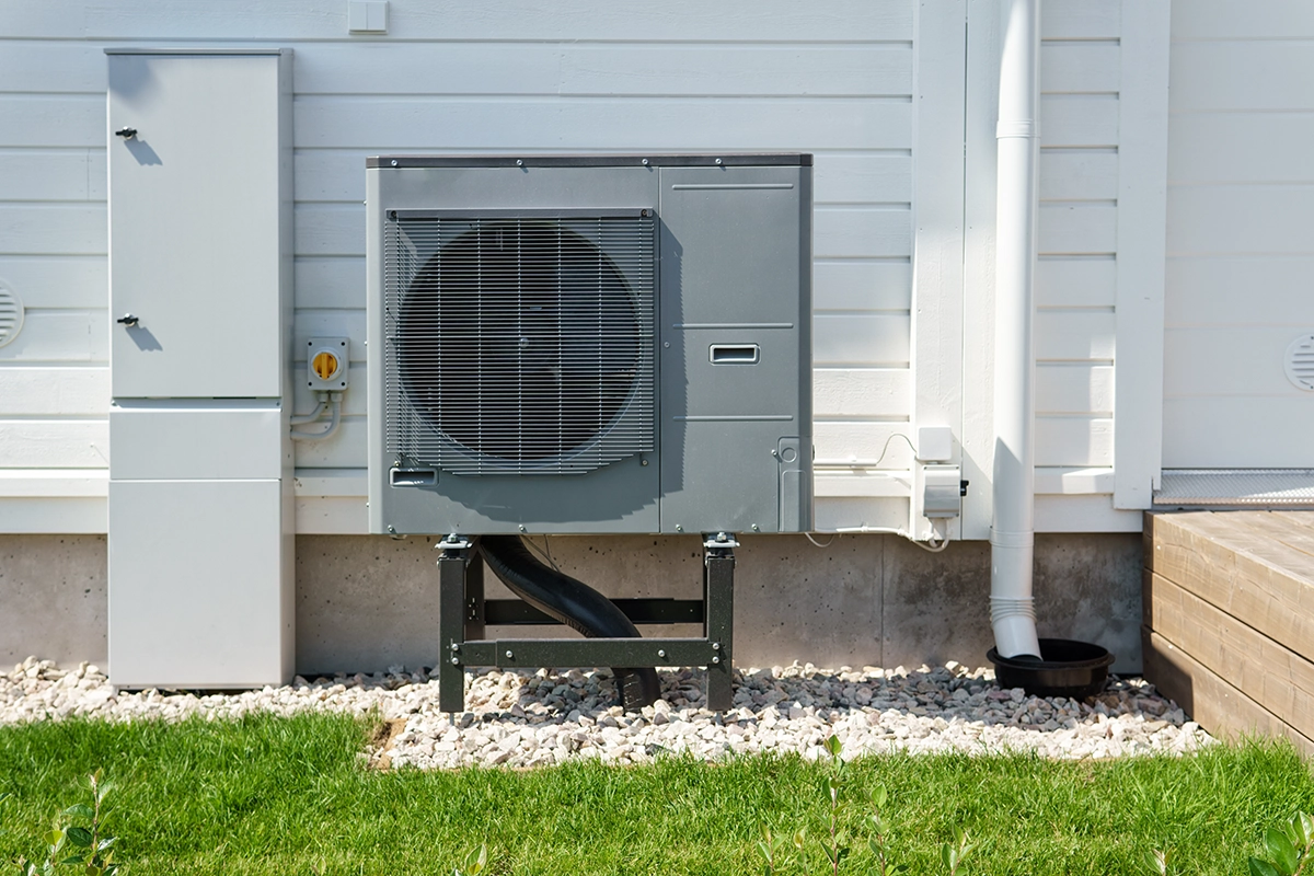 An outdoor heat pump condenser unit mounted on a concrete pad with gravel base next to a residential foundation. Best for blogs about heat pump systems, ductless outdoor units, heat pump installation, heat pump replacement, energy-efficient heating and cooling, and outdoor HVAC equipment.