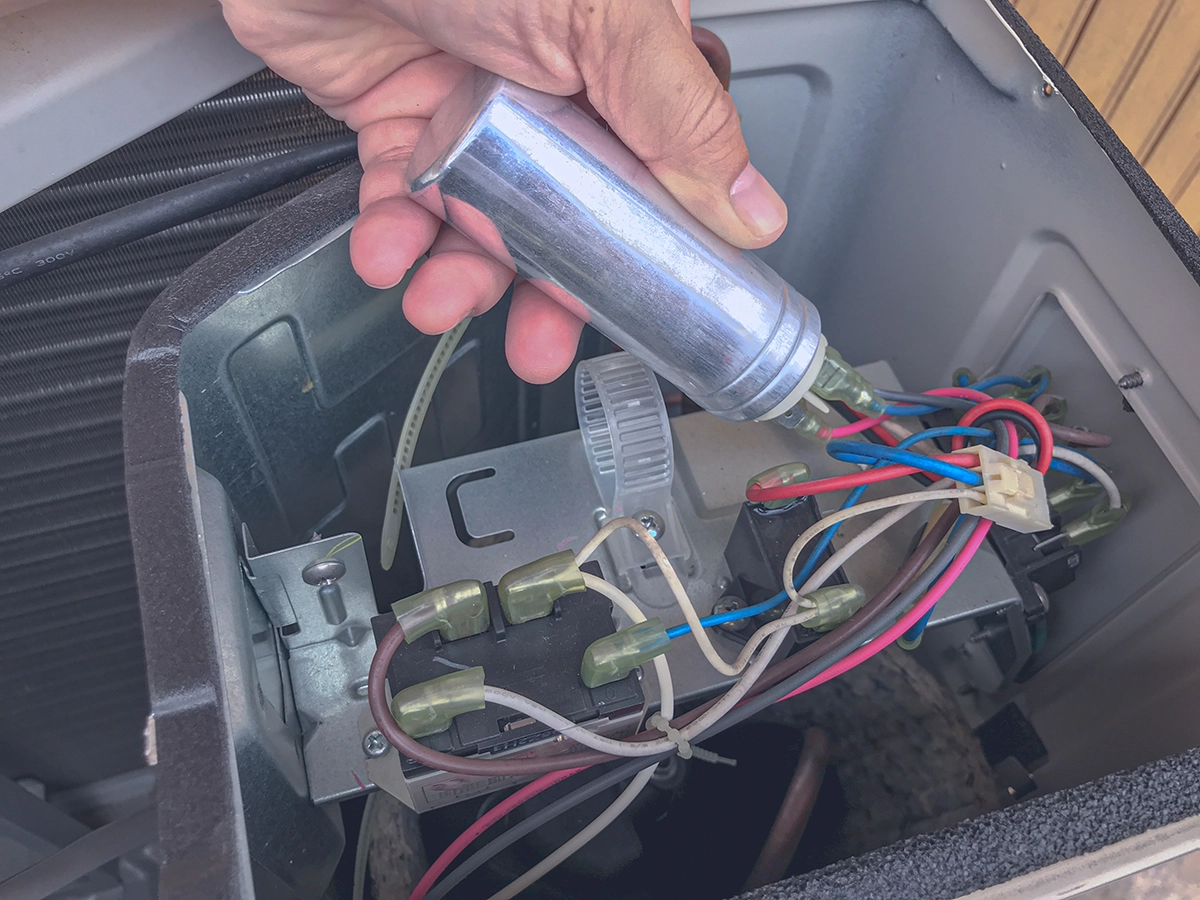 Technician replacing or inspecting an electrical capacitor inside an HVAC unit control compartment.