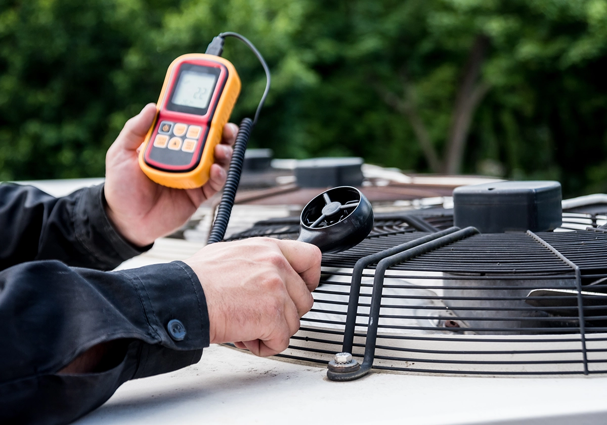 Technician using an anemometer to measure airflow at the top of an outdoor HVAC condenser unit. Best for blogs about AC maintenance inspections, condenser performance checks, HVAC diagnostic testing, why professional tune-ups matter, outdoor AC unit service, and airflow/ performance testing. Works best for diagnostic or maintenance-focused blogs.