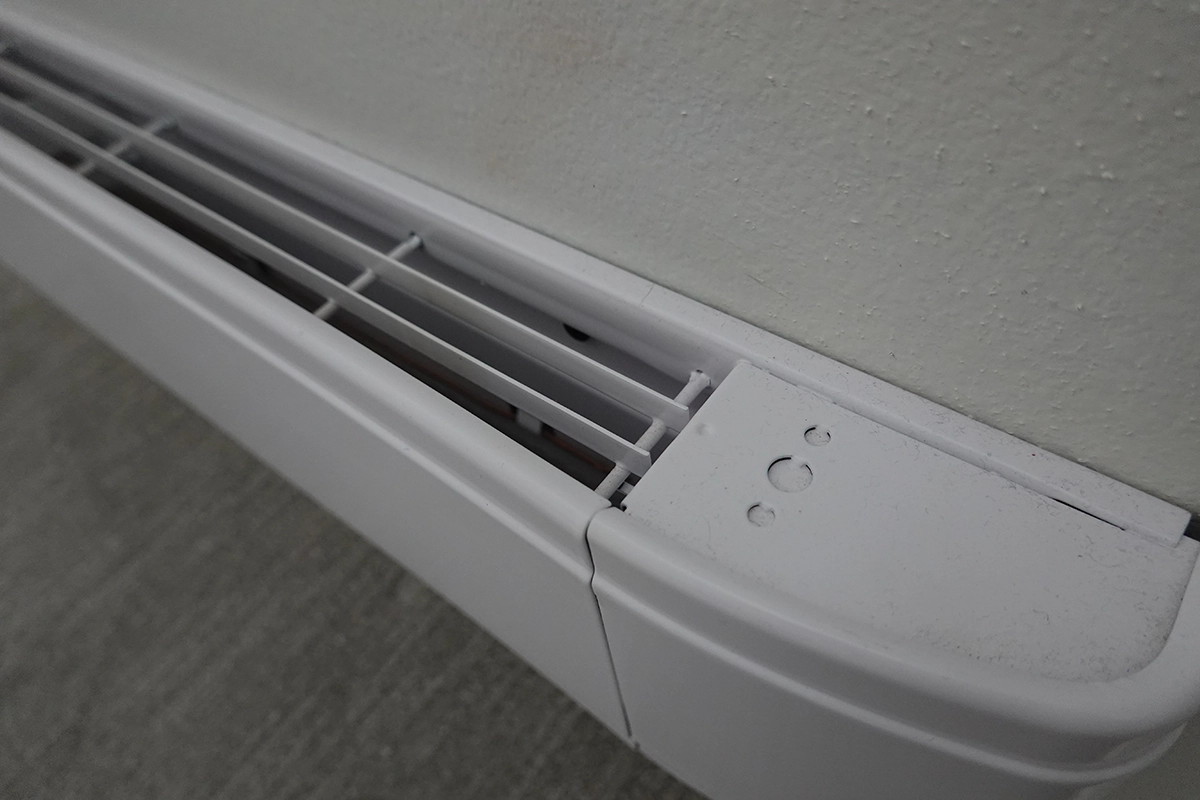 Close-up of a white electric baseboard heater installed along an interior wall. Best for blogs about baseboard heating, electric baseboard heaters, baseboard heater problems, heating options for homes, radiant vs forced-air heat, and room-by-room heating.