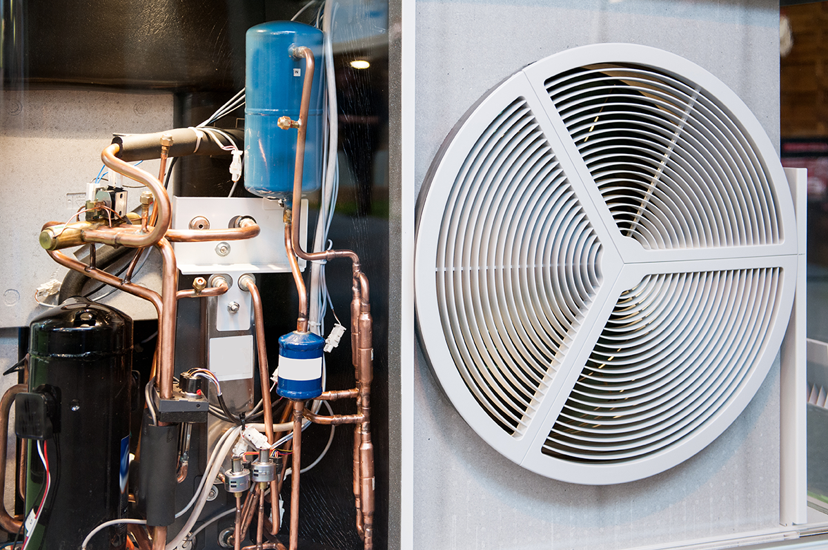 Cutaway view of heat pump equipment showing internal components, copper refrigerant lines, and the outdoor fan assembly. Best for blogs about heat pump components, AC system components, how a heat pump works, compressor and refrigerant system basics, heat pump repair.