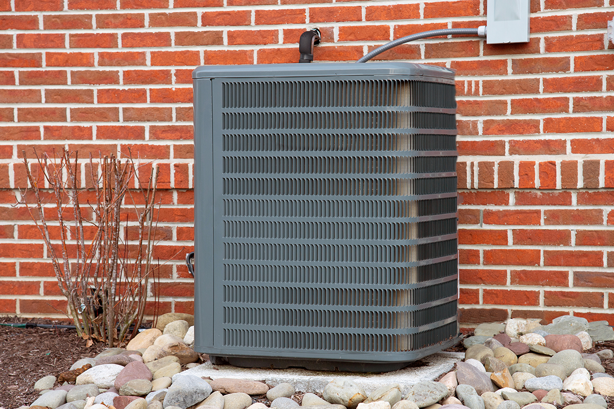 Residential outdoor AC condenser unit installed beside a brick wall with visible electrical connection. Best for blogs about air conditioning systems, AC replacement, condenser units, and residential cooling equipment.