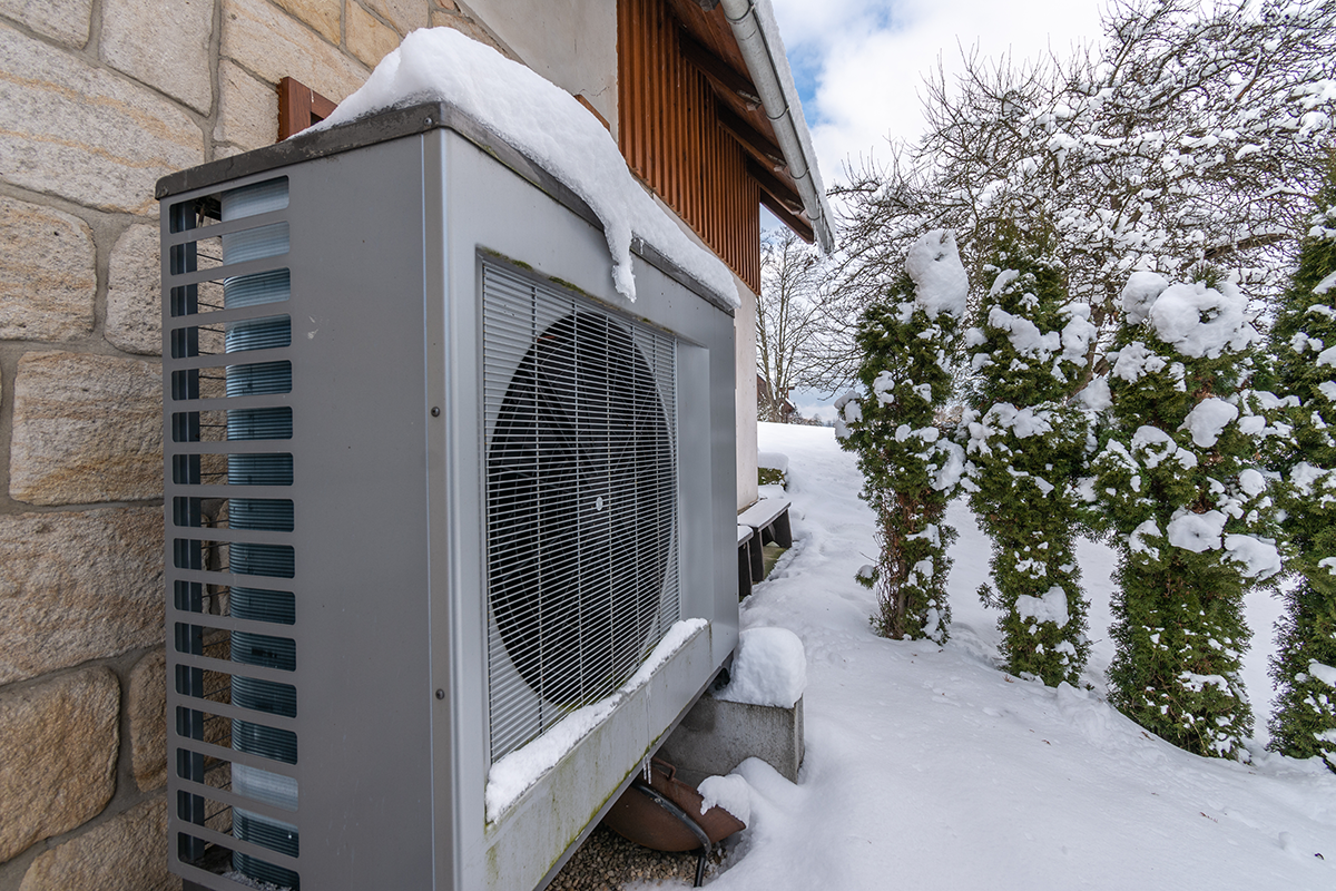 Outdoor heat pump unit installed beside a home in snowy winter conditions. Best for blogs about heat pump in winter, heat pump defrost cycle, winter HVAC performance, and cold-weather heat pump operation.