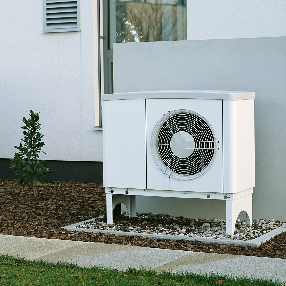 Outdoor heat pump unit installed on a raised stand beside a home. Best for blogs about heat pump systems, heat pump installation, heat pump replacement, cold-climate heat pumps, energy-efficient heating and cooling, and outdoor heat pump units.
