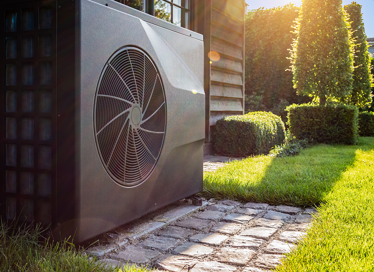 Outdoor heat pump unit installed beside a landscaped walkway and lawn.
