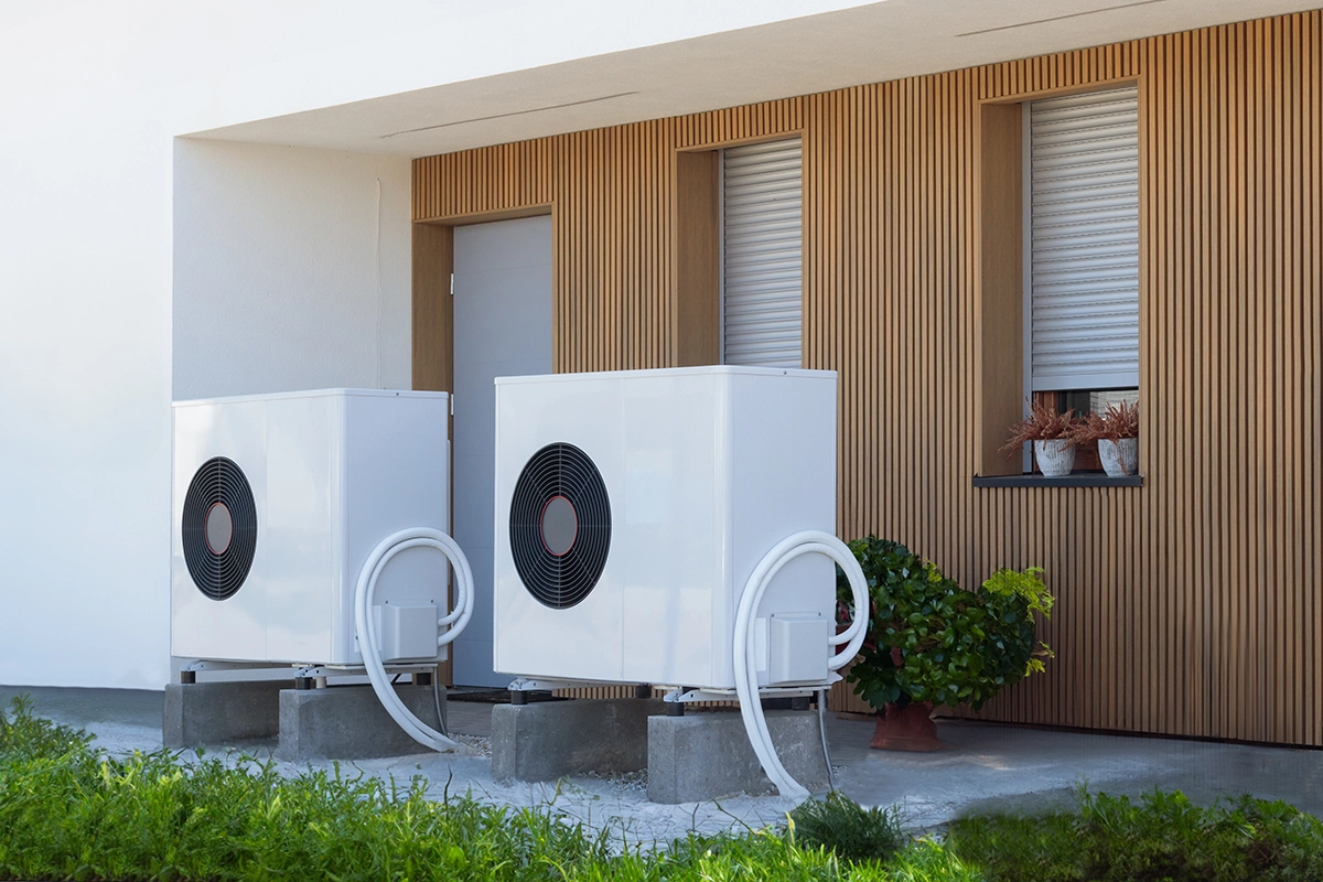 Two outdoor heat pump units installed on concrete pads beside a home. Best for blogs about heat pump installation, dual heat pump systems, multi-zone heating and cooling, energy-efficient home HVAC, outdoor heat pump equipment, and all-electric home comfort.
